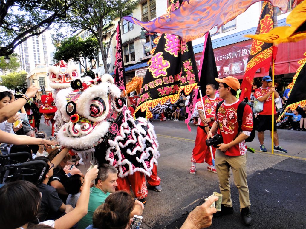 Brightly-colored Chinese lions dance down the street, taking money from outstretched hands in a Lunar New Year Parade. 